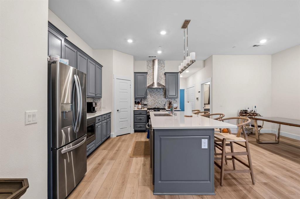 3781 Rochelle Court Prosper, TX 75078 - Photo 6 of 30 Kitchen with stainless steel refrigerator with ice dispenser, light wood finished floors, backsplash, pendant lighting, and an island with sink
