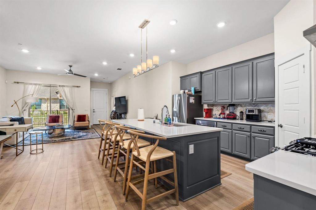 3781 Rochelle Court Prosper, TX 75078 - Photo 29 of 30 Kitchen featuring gray cabinets, open floor plan, a ceiling fan, a kitchen island with sink, and hanging light fixtures
