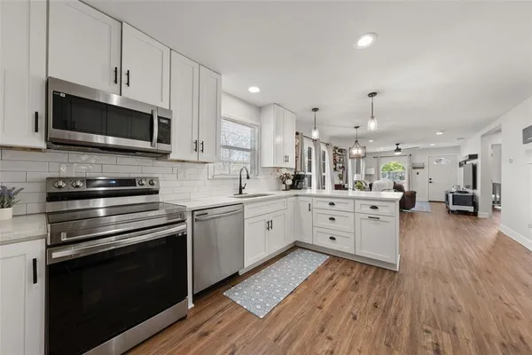 a kitchen with stainless steel appliances white cabinets a sink a stove a microwave and wooden floors