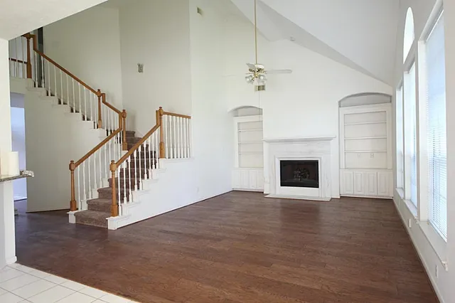 a view of an empty room with wooden floor fireplace and a window
