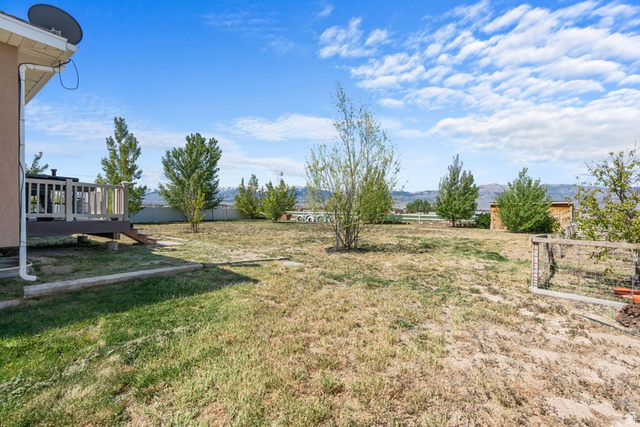 444 South Saddle Road Grantsville, UT 84029 - Photo 30 of 33 Expansive backyard featuring a wood deck, mature trees, partial fencing, and a distant mountain backdrop