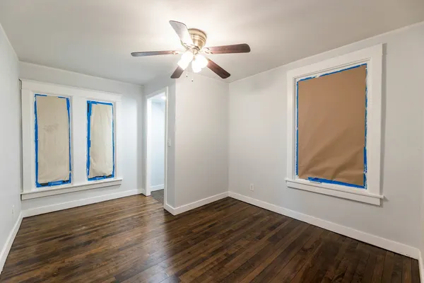 an empty room with wooden floor chandelier fan and windows