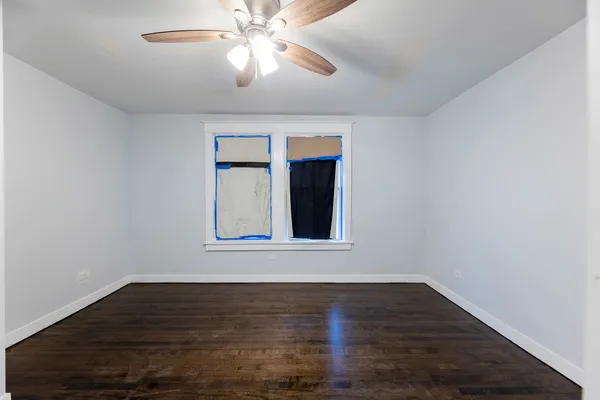 a view of an empty room with wooden floor and a ceiling fan