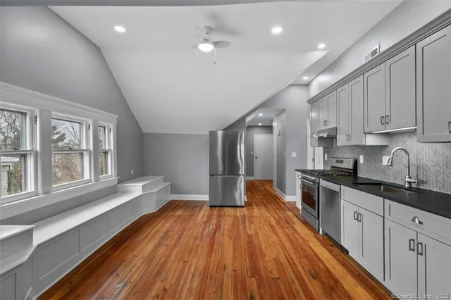 a large kitchen with stainless steel appliances a large window a oven and white cabinets with wooden floor