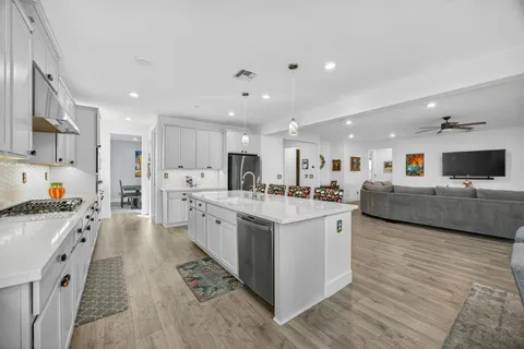 a large white kitchen with stainless steel appliances kitchen island a stove a refrigerator a oven and white cabinets
