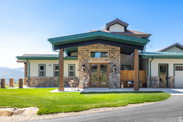 6117 North Rocky Ridge Road Peoa, UT 84061 - Photo 25 of 82 Stone facade entry featuring substantial wood columns, double wooden doors with X-panel detailing, and a prominent green roofline