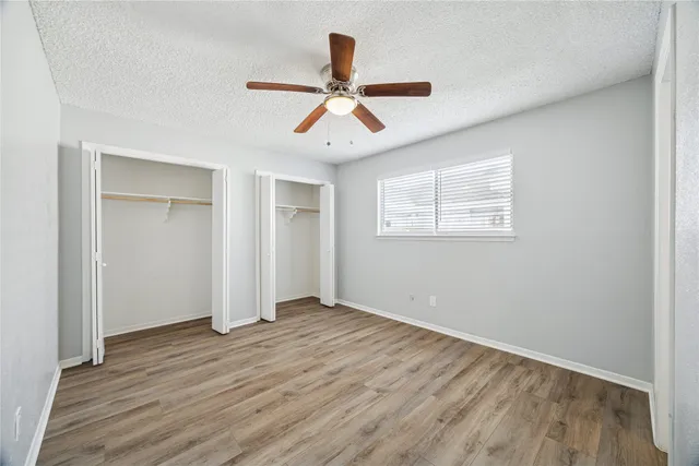 an empty room with wooden floor ceiling fan and windows