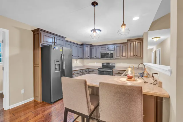 a kitchen with stainless steel appliances granite countertop a refrigerator a sink dishwasher a stove a dining table and chairs with wooden floor