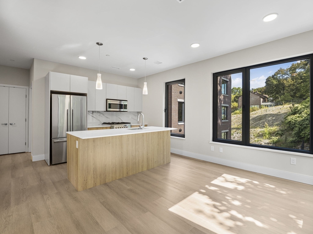 249 Corey Road, Unit 309 Boston, MA 02135 - Photo 7 of 29 a large kitchen with stainless steel appliances granite countertop a refrigerator a sink dishwasher a stove and white countertops with wooden floor