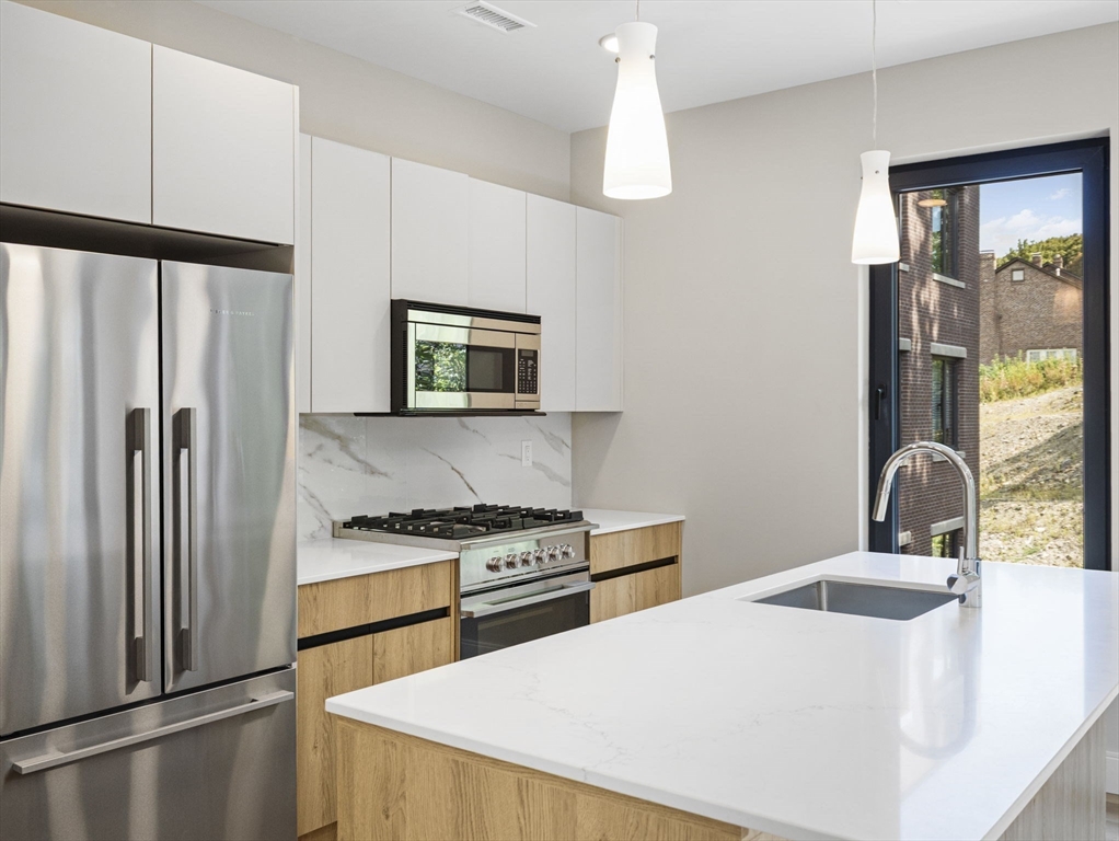 249 Corey Road, Unit 309 Boston, MA 02135 - Photo 9 of 29 a kitchen with stainless steel appliances a refrigerator a stove a sink and a refrigerator with wooden floor