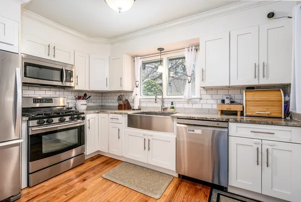 a kitchen with granite countertop white cabinets appliances a sink and a window