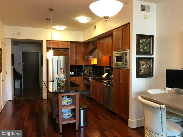 a kitchen with stainless steel appliances granite countertop a refrigerator a stove top oven and a dining table with wooden floor