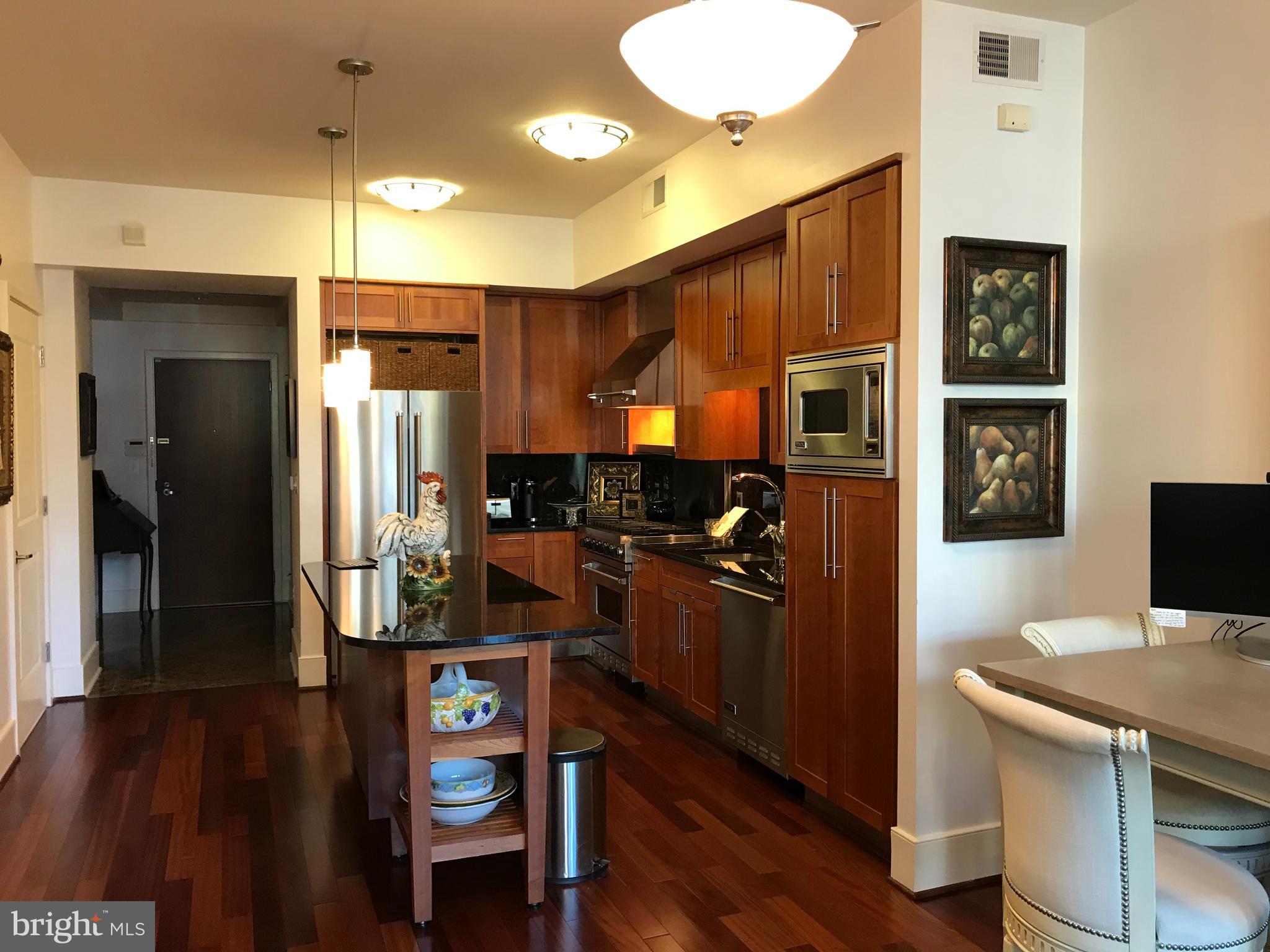 4301 Military Road Northwest, Unit 208 Washington, DC 20015 - Photo 3 of 32 a kitchen with stainless steel appliances granite countertop a refrigerator a stove top oven and a dining table with wooden floor