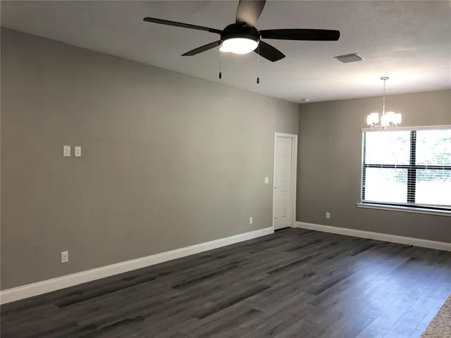 an empty room with wooden floor ceiling fan and windows