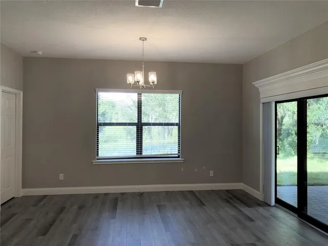 an empty room with wooden floor chandelier and windows