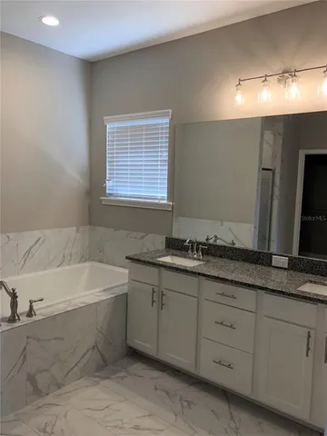 a bathroom with a granite countertop bathtub a sink and a large mirror