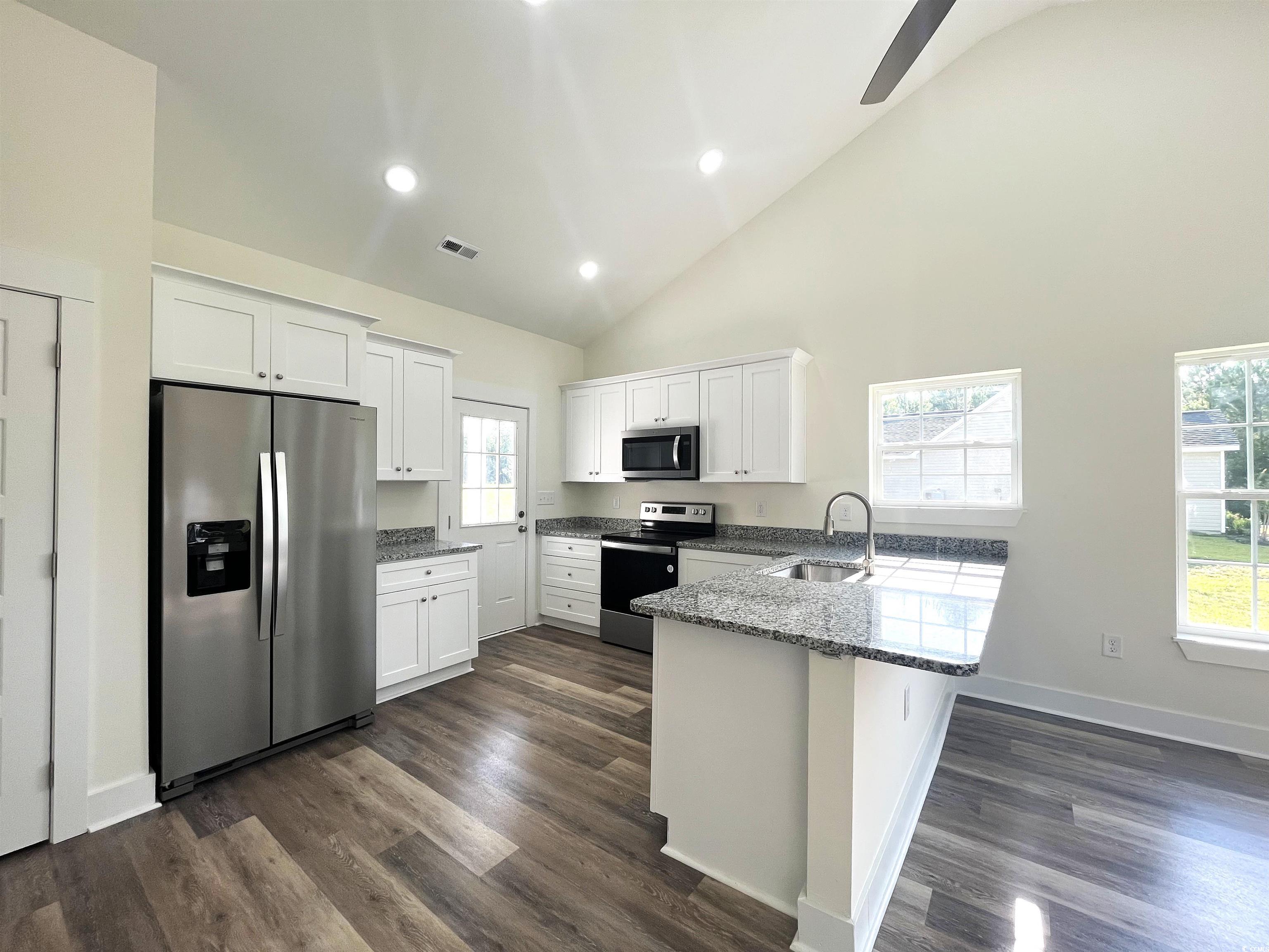 1174 St John Road Galivants Ferry, SC 29544 - Photo 6 of 22 Kitchen featuring stainless steel appliances, a peninsula, white cabinetry, dark stone countertops, and high vaulted ceiling