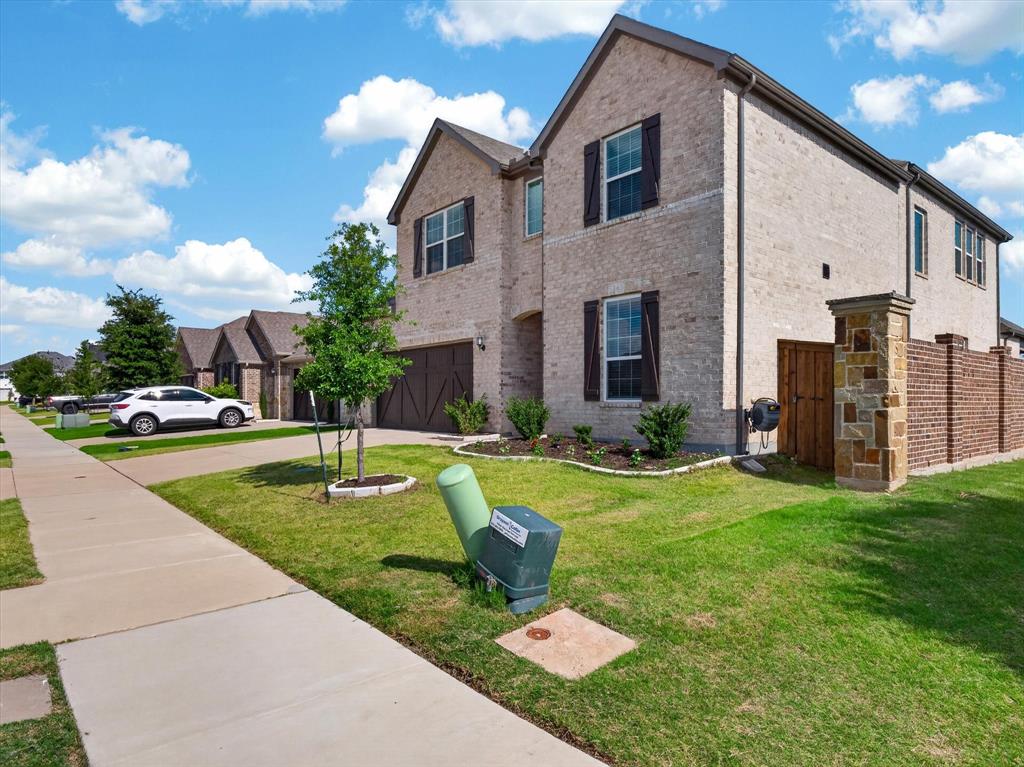 636 Corner Post Path Celina, TX 75009 - Photo 36 of 40 Two-story brick exterior featuring dark shutters, an attached garage with a dark wood-finish door, and a stone and brick privacy fence