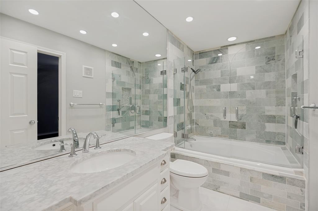 Spacious bathroom featuring a full-length mirror, double vanity with stone countertop, and a shower-over-tub combination with glass enclosure