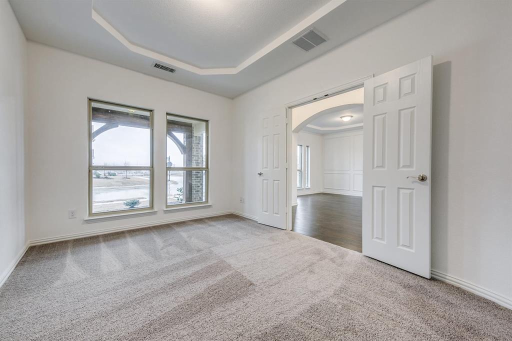 104 Sweetleaf Drive Red Oak, TX 75154 - Photo 26 of 36 A spacious room featuring soft gray carpeting, a tray ceiling, and two large windows offering views of the outdoors