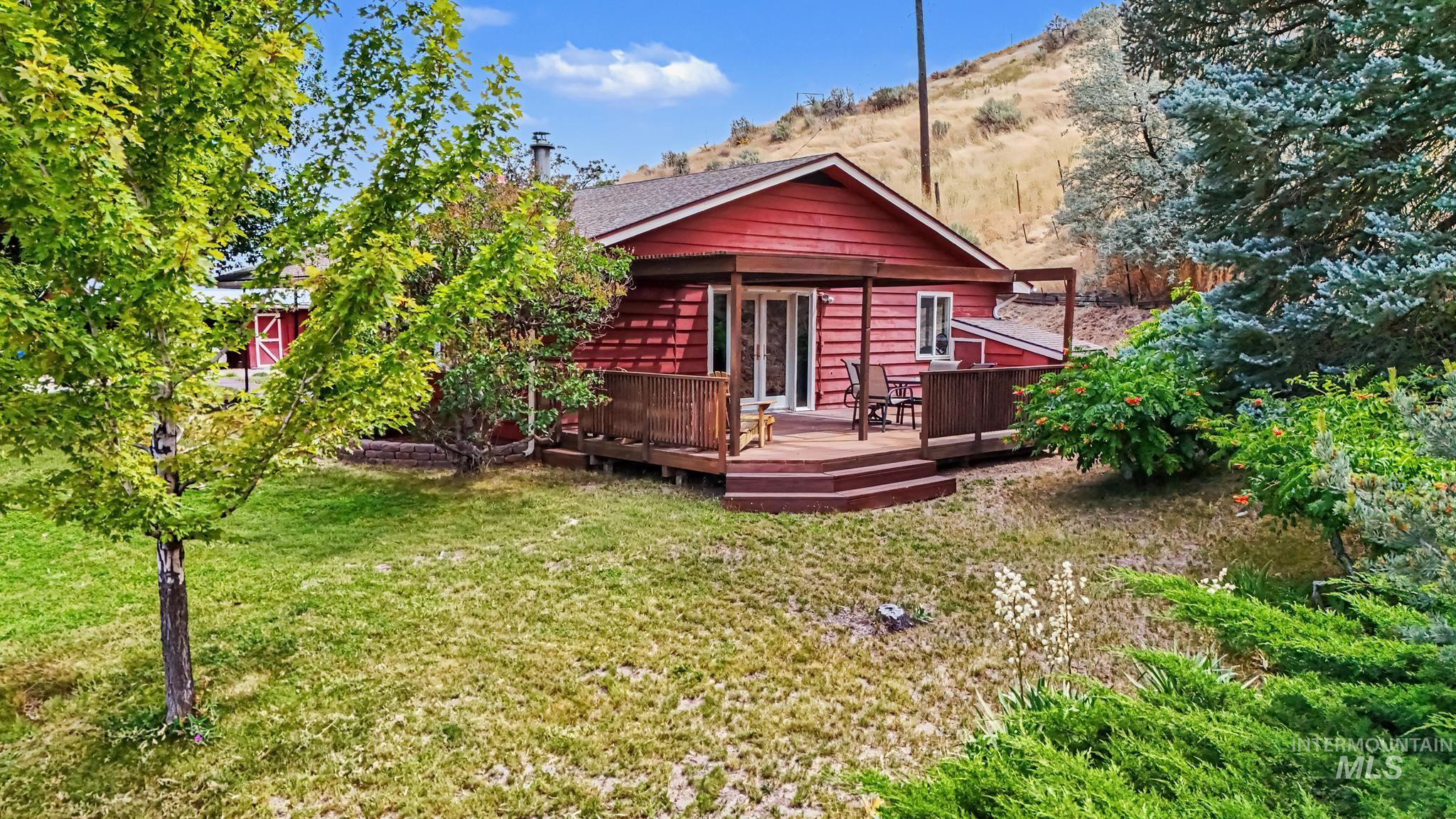 4311 Frozen Dog Road Emmett, ID 83617 - Photo 2 of 31 Red siding exterior with a wood deck, double glass doors, and a sloped terrain backdrop