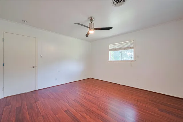 an empty room with wooden floor ceiling fan and windows