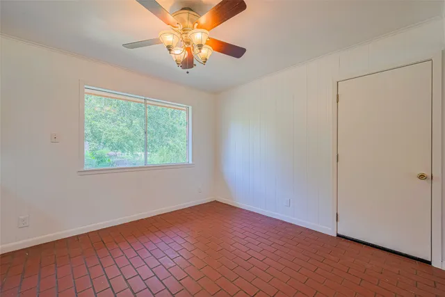an empty room with wooden floor chandelier fan and windows