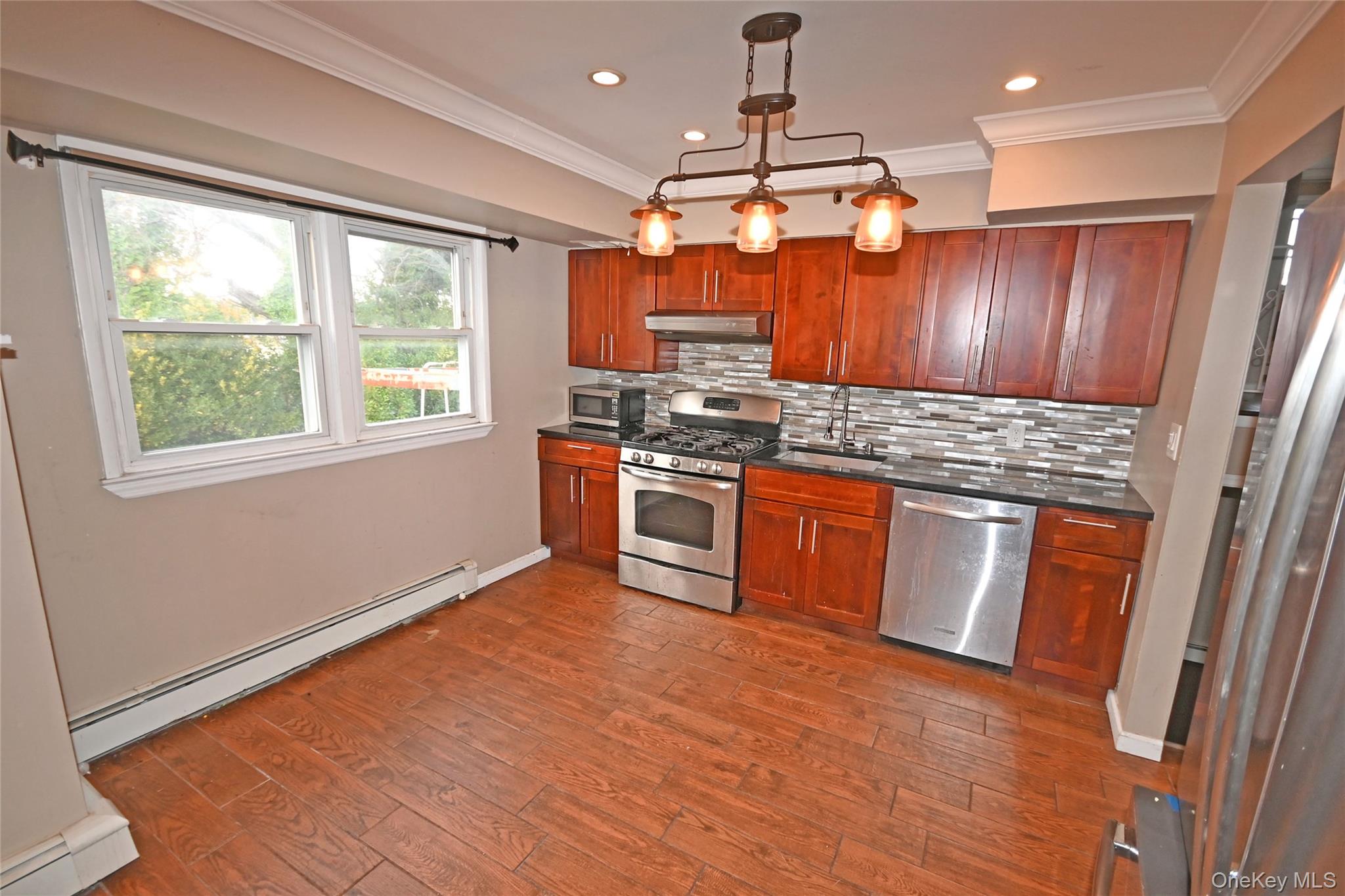 89 Osborne Road West Hempstead, NY 11552 - Photo 31 of 50 Kitchen with a baseboard radiator, appliances with stainless steel finishes, decorative light fixtures, dark wood-style flooring, and decorative backsplash