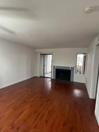 an empty room with wooden floor fireplace and windows