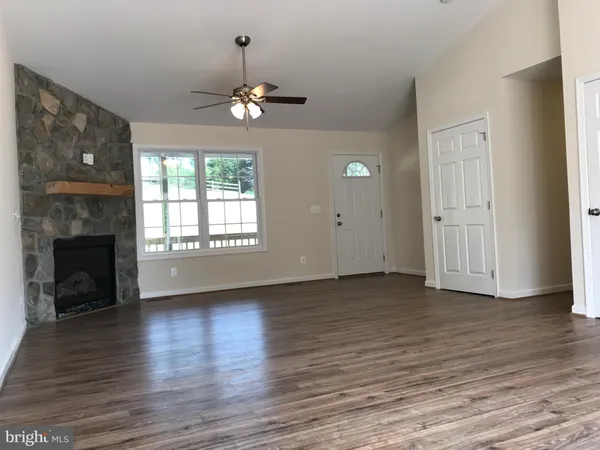 a view of an empty room with wooden floor fireplace and a window