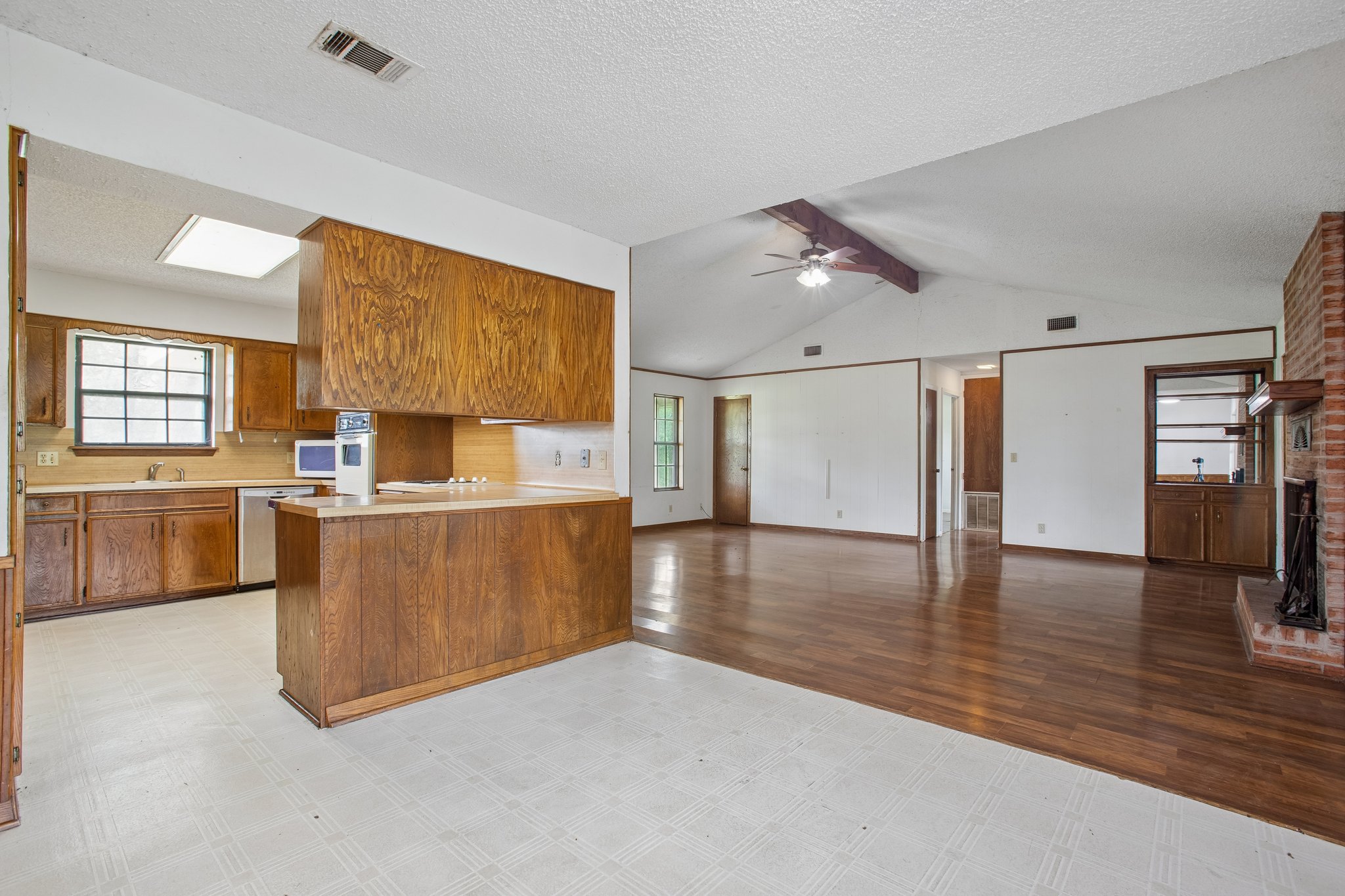 406 Monkey Road Elgin, TX 78621 - Photo 9 of 39 Kitchen and living space featuring a partial wall with wood-finish paneling, wood-finish cabinetry, a skylight, a vaulted ceiling with exposed beam, and a brick fireplace