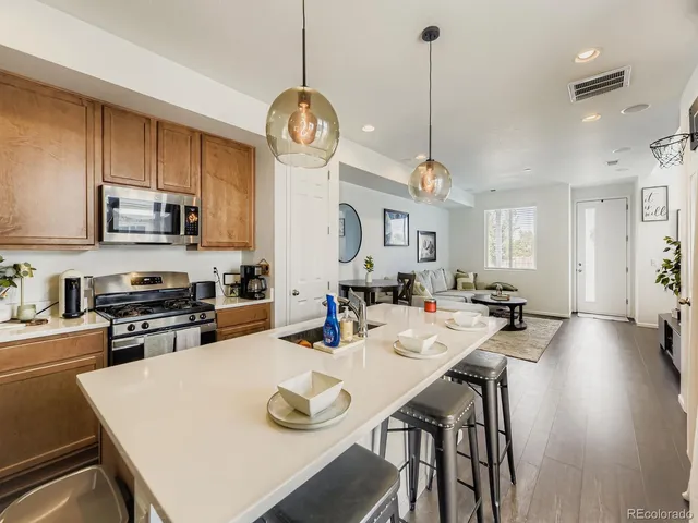 a open kitchen with stainless steel appliances granite countertop a stove top oven a refrigerator a sink dishwasher a dining table and chairs with wooden floor