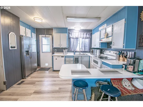 a kitchen with stainless steel appliances kitchen island granite countertop a refrigerator a sink dishwasher and white cabinets with wooden floor