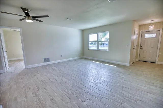an empty room with wooden floor fan and windows