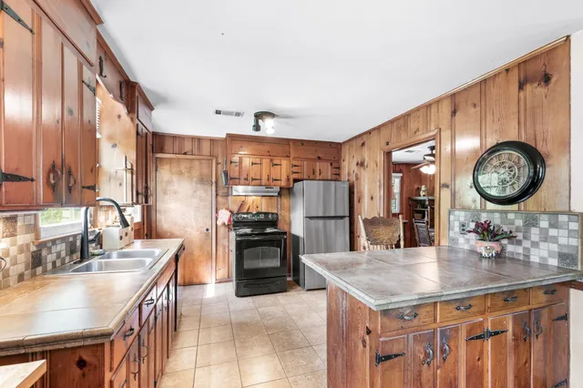 a kitchen with granite countertop a sink a stove top oven a clock and cabinets