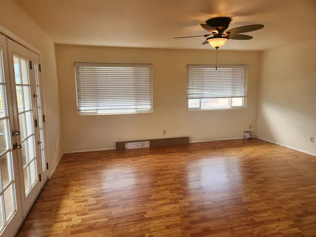 an empty room with wooden floor chandelier fan and windows