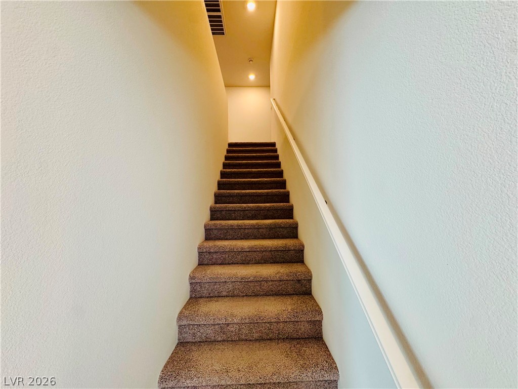 9249 Innot Avenue Las Vegas, NV 89148 - Photo 8 of 24 A gracefully carpeted stairway leads upwards, illuminated by subtle recessed lighting.