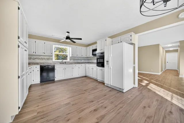 a kitchen with granite countertop a refrigerator oven a sink dishwasher and white cabinets with wooden floor