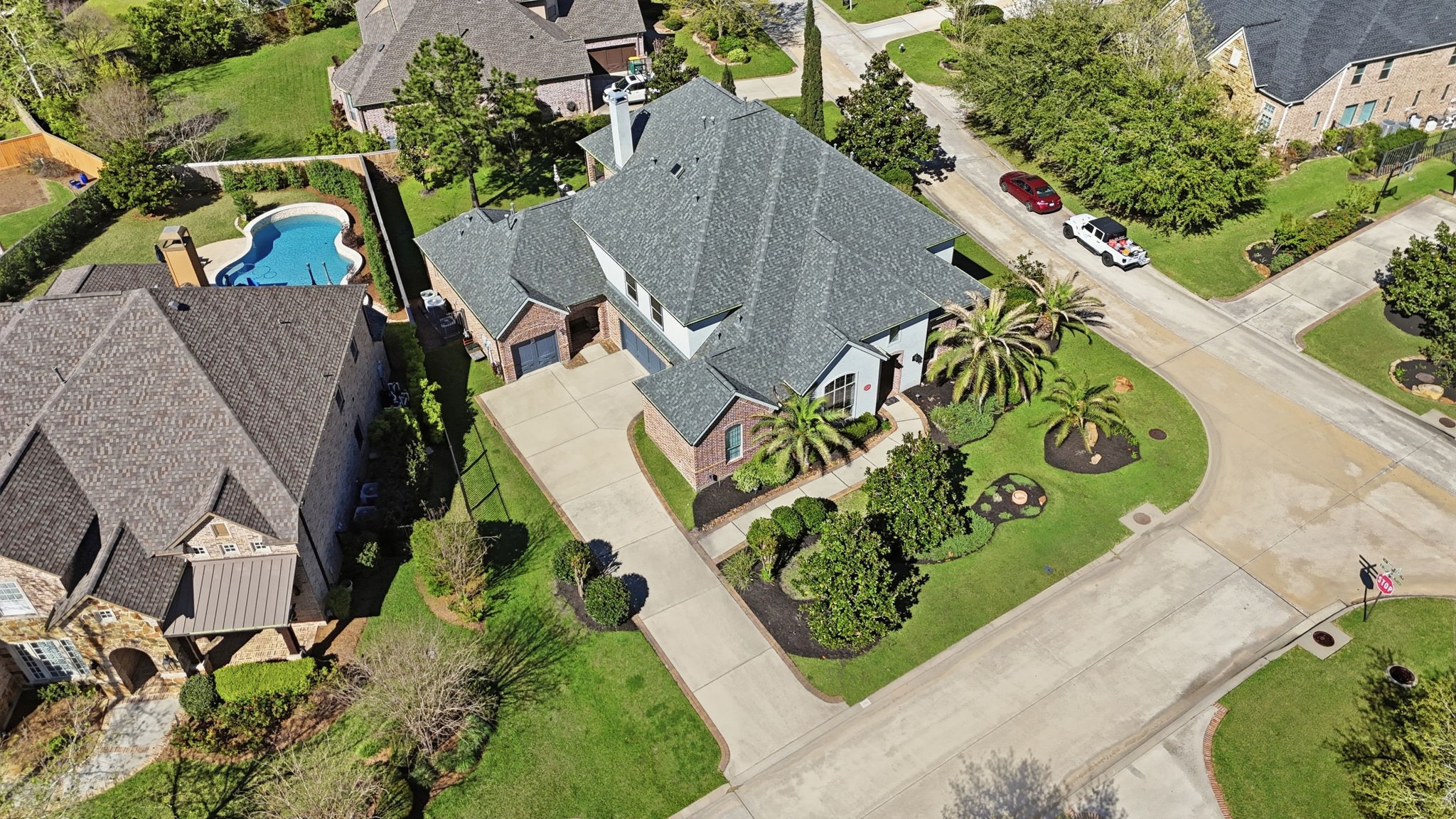 223 South Bauer Point Circle Spring, TX 77389 - Photo 41 of 50 This aerial view showcases a spacious, elegant two-story home with a well-maintained yard and lush landscaping, situated on a corner lot. The property features modern architecture and a large driveway, with a neighboring house that includes a swimming pool. The neighborhood appears quiet and residential, with tree-lined streets.