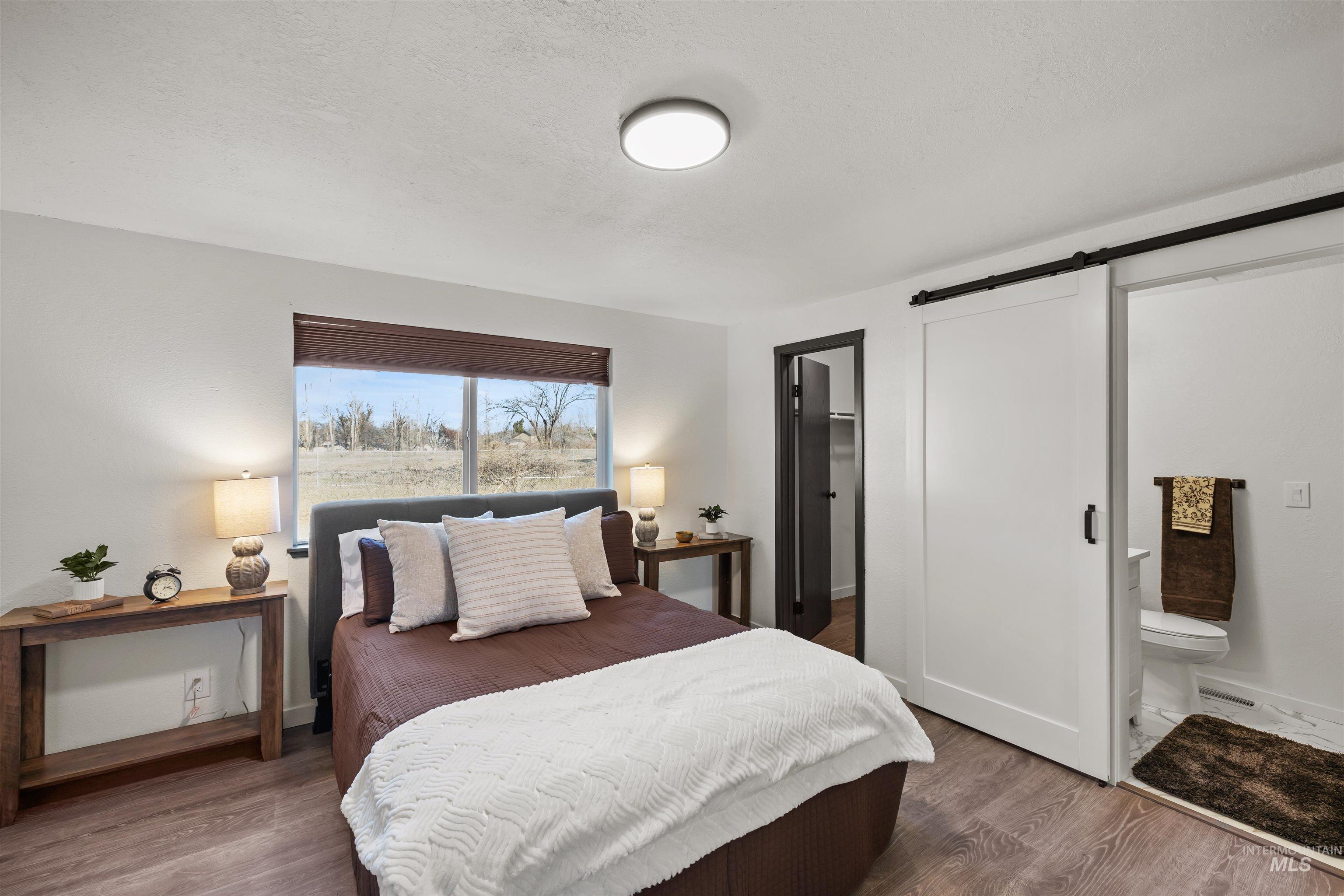 3154 South McCormick Way Boise, ID 83709 - Photo 12 of 50 Bedroom with wood finished floors, a walk in closet, a barn door, ensuite bathroom, and a textured ceiling