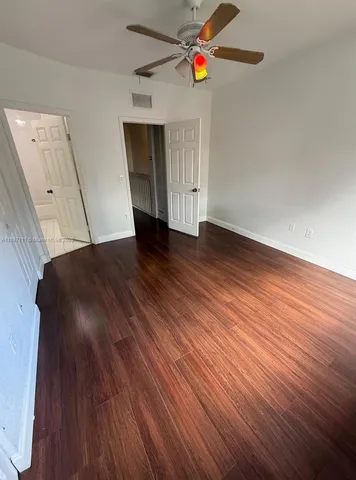 a view of an empty room with wooden floor and a ceiling fan