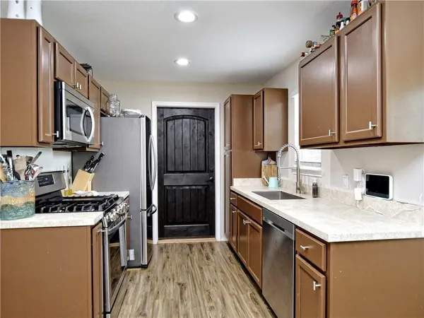 a kitchen with stainless steel appliances granite countertop a stove a sink dishwasher a refrigerator and wooden cabinets with wooden floor