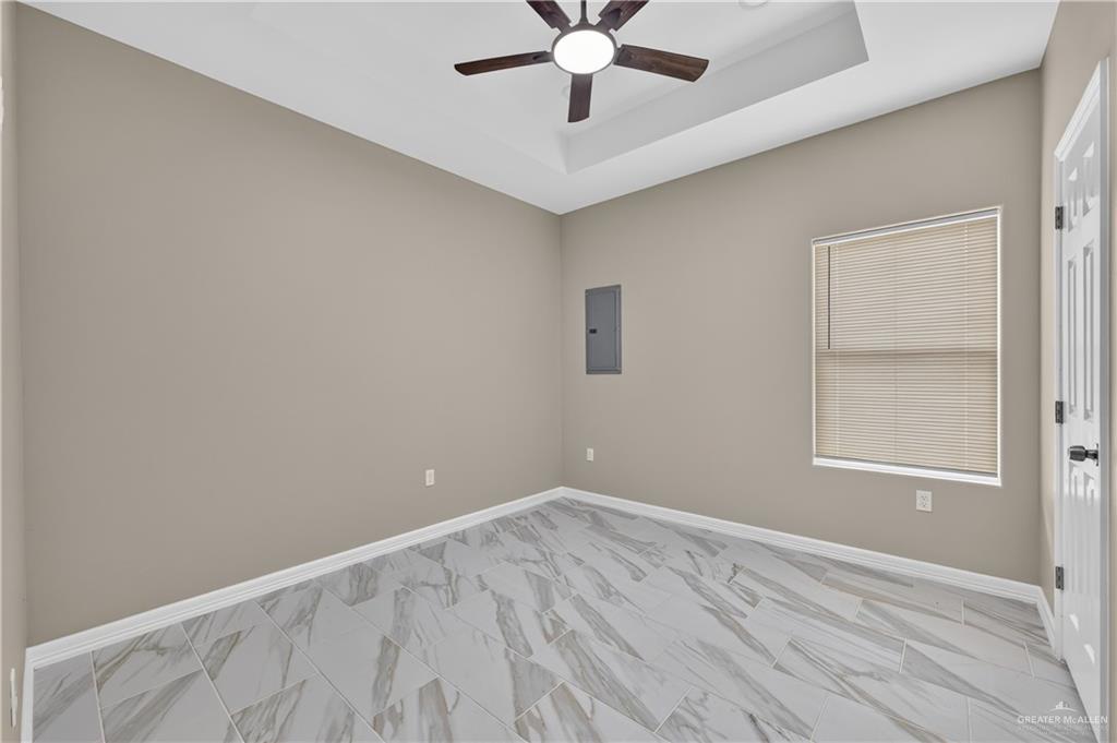 1920 Trinity Street Donna, TX 78537 - Photo 14 of 23 Contemporary room featuring light gray walls, gray and white marble-look tile flooring, and a vaulted tray ceiling with a dark wood-finish ceiling fan