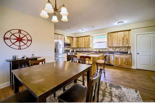 a kitchen with stainless steel appliances granite countertop a stove a refrigerator a dining table and chairs with wooden floor