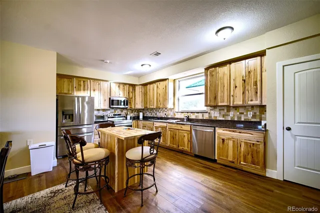a kitchen with stainless steel appliances granite countertop a stove a refrigerator a kitchen island and chairs in it