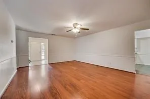 a view of an empty room with wooden floor and a ceiling fan