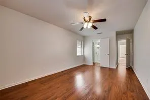 a view of an empty room with wooden floor and a ceiling fan