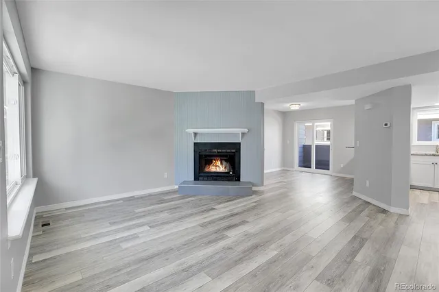 a view of an empty room with wooden floor fireplace and a window