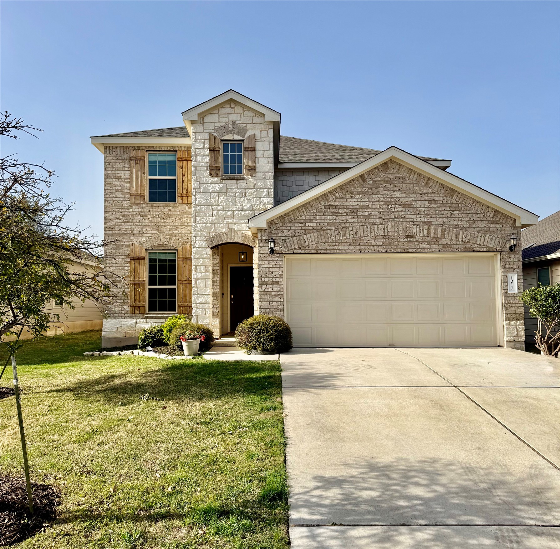View of front facade featuring a front lawn, stone siding, an attached garage, driveway, and brick siding