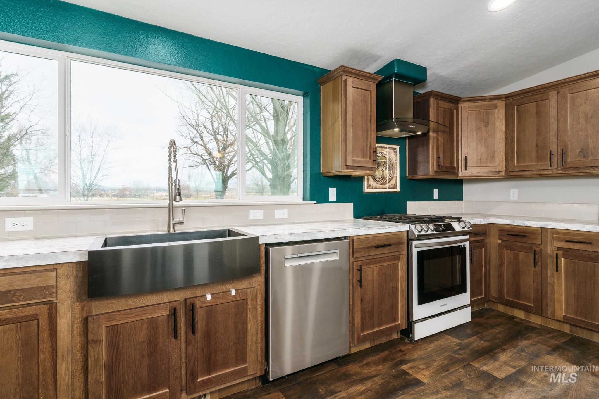 13678 North Hawthorne Road Pocatello, ID 83202 - Photo 4 of 37 Kitchen featuring appliances with stainless steel finishes, wall chimney range hood, light countertops, lofted ceiling, and dark wood-type flooring